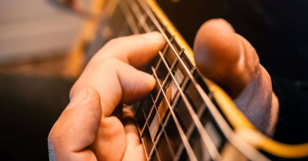 A man is sitting down playing a Gibson Les Paul. A blurry acoustic guitar is in the background.